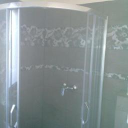 Przedsiębiorstwo Remontowo-Budowlane Robert Nowodworski - Szklana kabina prysznicowa z chromowanymi detalami na tle ciemnych, wzorzystych płytek w łazience. Widoczna bateria i uchwyty. Wykończona łazienka po remoncie.