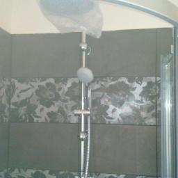 Przedsiębiorstwo Remontowo-Budowlane Robert Nowodworski - Szara kabina prysznicowa z kwiatowym motywem na płytkach. Nowa słuchawka prysznicowa z folią ochronną. Widok na fragment łazienki po remoncie.