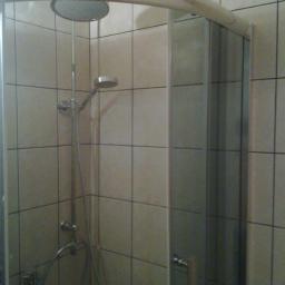 Przedsiębiorstwo Remontowo-Budowlane Robert Nowodworski - Kabina prysznicowa z deszczownicą i szklanymi drzwiami w łazience wyłożonej beżowymi, kwadratowymi płytkami ceramicznymi. Widoczne elementy armatury.