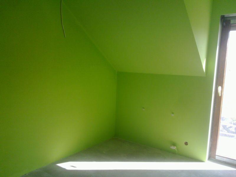Pomalowane na jaskrawy zielony kolor poddasze z oknem, widoczne gniazdka i kabel. Świeżo odnowione wnętrze w odcieniach zieleni.
