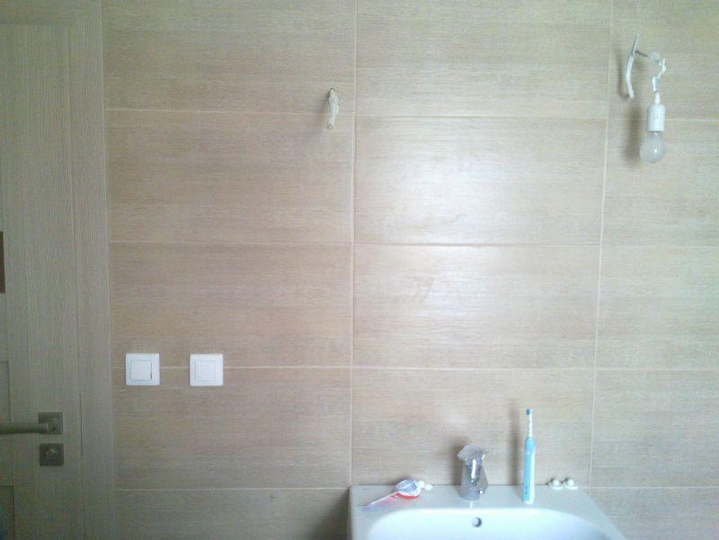 Wykończona łazienka w odcieniach beżu w Poznaniu: płytki imitujące drewno na ścianach, biała armatura, włączniki światła i wisząca żarówka. Minimalistyczny design.