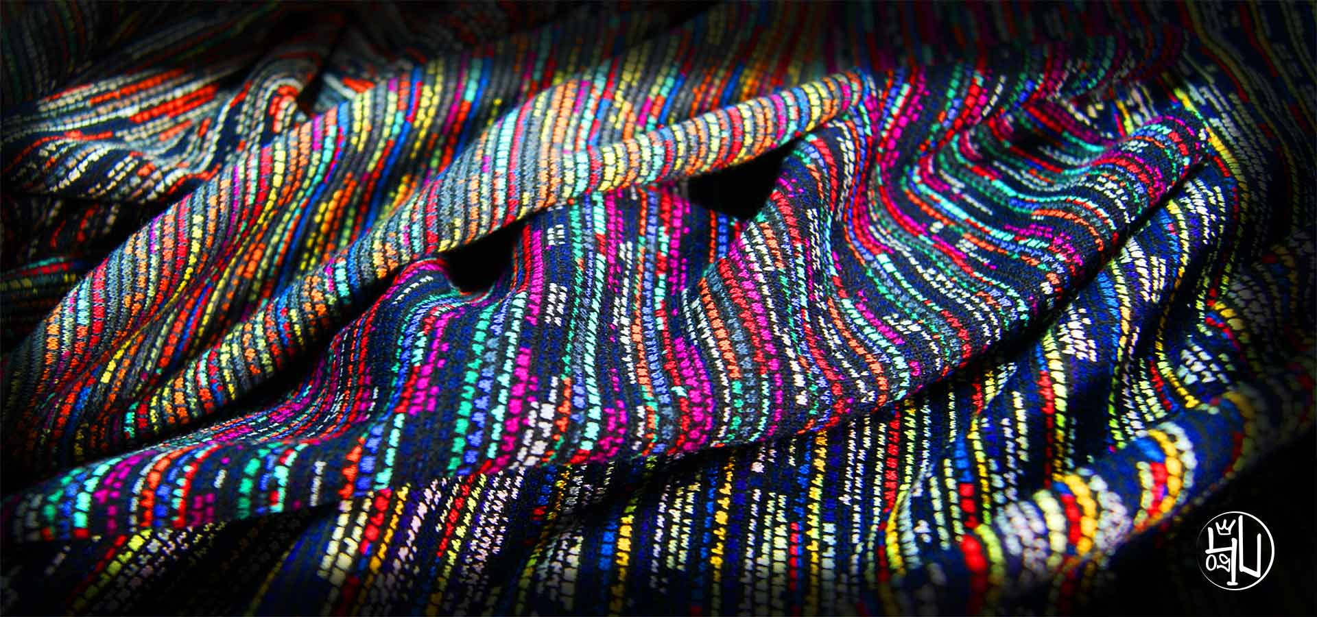 Płaski żakard o gęstym splocie z wielobarwnymi, pionowymi paskami w odcieniach czerwieni, niebieskiego, zieleni, żółci i bieli, ułożony w miękkie fałdy.