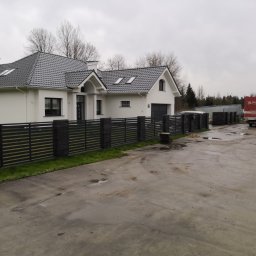 Tonda Zakład Budowlany Krzysztof Koń - Nowoczesny dom murowany z szarą dachówką i ciemnym ogrodzeniem panelowym, widoczny w pochmurny dzień, z ciężarówką firmy budowlanej w tle.