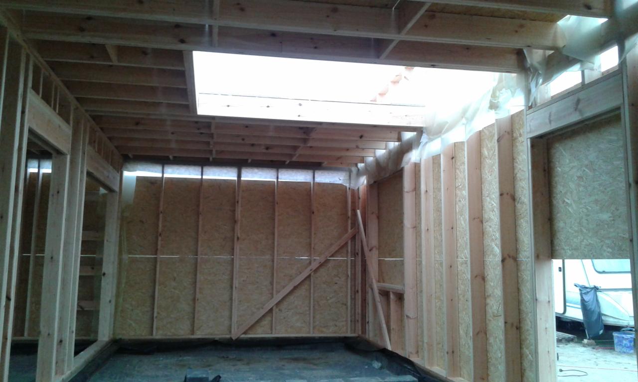 Wnętrze w trakcie budowy: szkielet ścian z drewna i płyty OSB, widoczne okno dachowe i otwory drzwiowe. Etap prac wykończeniowych, surowy stan.