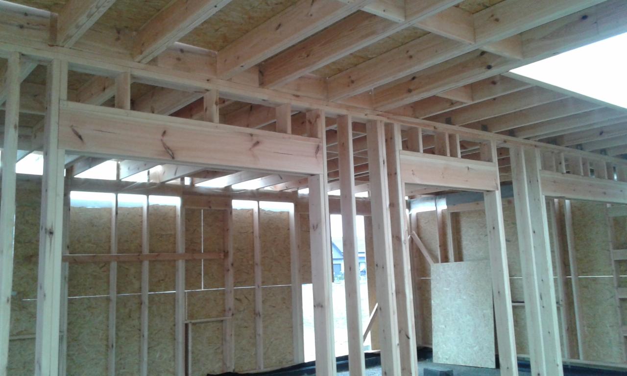 Drewniana konstrukcja szkieletowa domu w trakcie budowy, widok od wewnątrz. Elementy z płyty OSB. Naturalne oświetlenie wpada przez otwory okienne.