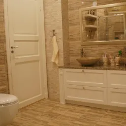 Jasna łazienka z beżowymi płytkami, dużym lustrem i dwiema umywalkami w kolorze piasku. Widoczna kabina prysznicowa i biała szafka pod umywalką.