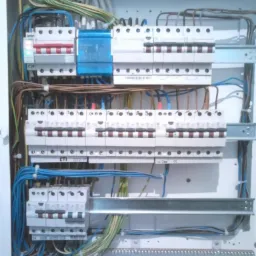 Rozdzielnia elektryczna z zainstalowanymi bezpiecznikami i okablowaniem, widoczne różne kolory przewodów i elementy mocujące.