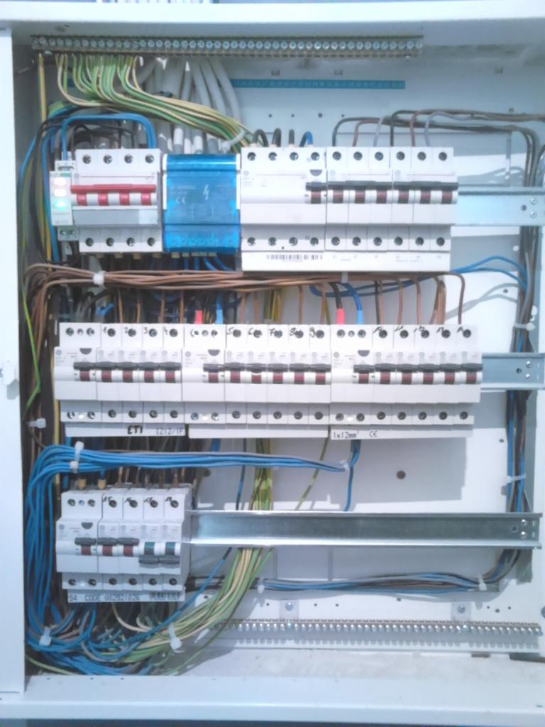 Rozdzielnia elektryczna z zainstalowanymi bezpiecznikami i okablowaniem, widoczne różne kolory przewodów i elementy mocujące.