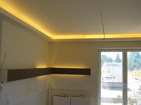 Wykończone wnętrze z oświetleniem LED w suficie i na ścianie, widoczne okno z widokiem na zewnątrz i fragment instalacji. Ciepłe, nastrojowe światło.