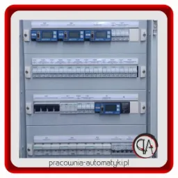 Rozdzielnica elektryczna z bezpiecznikami i wyświetlaczami Janitza, widok z przodu, szara obudowa, etykiety opisujące obwody, instalacja elektryczna wewnątrz.