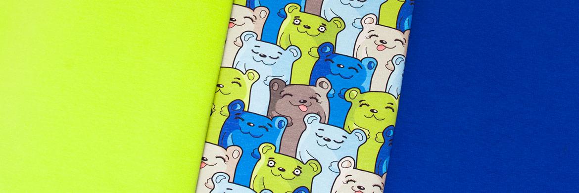 Kolorowe tkaniny: neonowo-zielona, niebieska i wzorzysta z motywem uśmiechniętych misiów w odcieniach niebieskiego, zielonego i szarego.