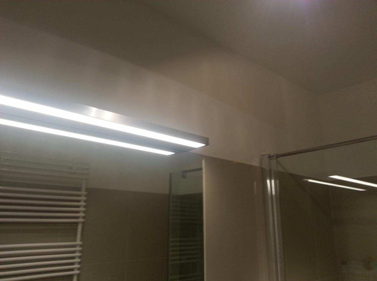 Nowoczesna łazienka po remoncie: szklana kabina prysznicowa, grzejnik drabinkowy i podwójne oświetlenie LED w minimalistycznym stylu. Ujęcie z dołu.