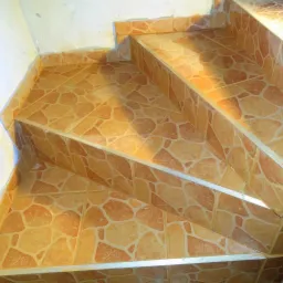 Wykończone schody z brązowych płytek o nieregularnym wzorze, zabezpieczone srebrnymi listwami. Widok z góry, dobre oświetlenie.