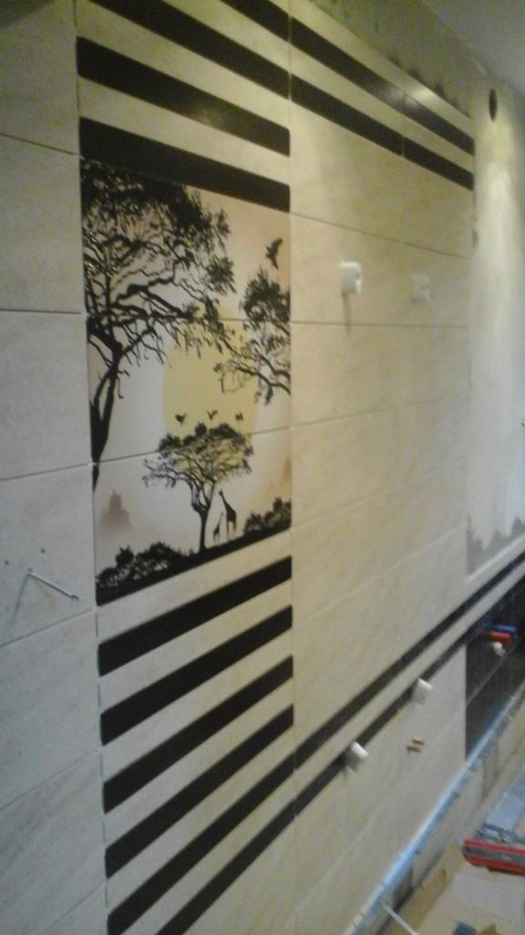 Ściana wyłożona jasnymi płytkami z motywem zebry i afrykańskiej sawanny. Dekoracyjne wykończenie łazienki z akcentem podróżniczym.