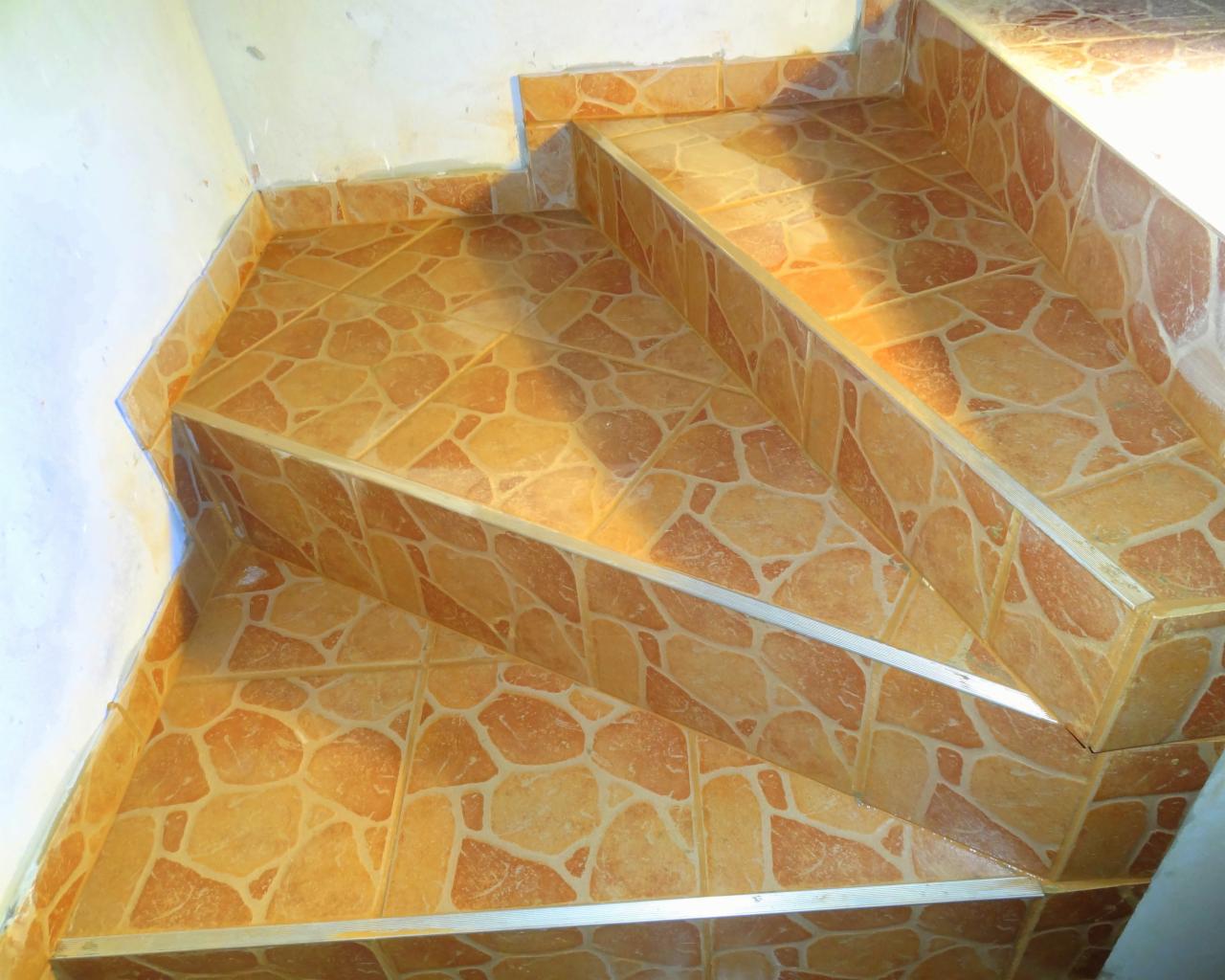 Wykończone schody z brązowych płytek o nieregularnym wzorze, zabezpieczone srebrnymi listwami. Widok z góry, dobre oświetlenie.