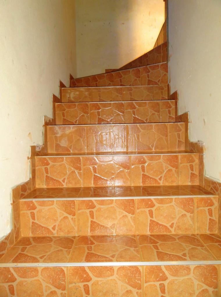 Wykończone schody wewnątrz budynku, pokryte pomarańczowo-brązowymi płytkami imitującymi kamień. Widoczne białe ściany i srebrne listwy na krawędziach stopni.