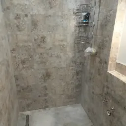 Ukończona kabina prysznicowa z szarymi, wzorzystymi płytkami ceramicznymi na ścianach i podłodze, wyposażona w deszczownicę, p&oacute;łkę na kosmetyki i odpływ liniowy.