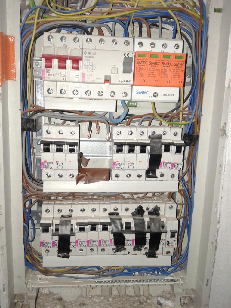 Rozdzielnia elektryczna z zabezpieczeniami przepięciowymi Simtec, widok z bliska. W tle widoczne przewody. Zabezpieczenia częściowo zaklejone taśmą.
