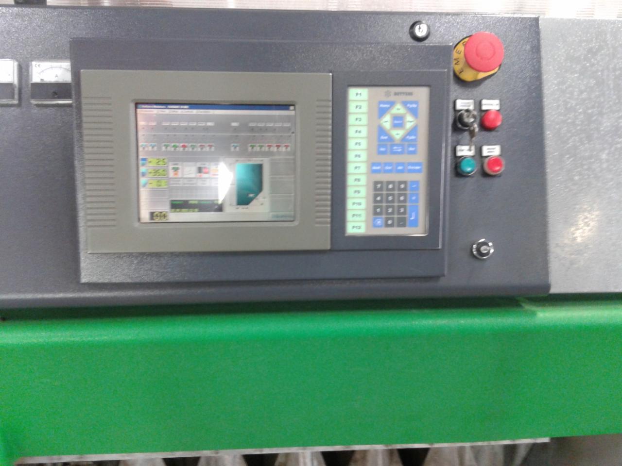 Panel sterowania maszyny z ekranem LCD, przyciskami funkcyjnymi i awaryjnymi. Szary panel na zielonej obudowie. Widoczne wskaźniki i klawiatura numeryczna.