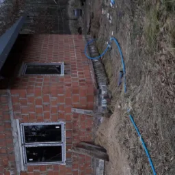 Niedokończony budynek z czerwonej cegły z oknami i czarnym dachem na zewnątrz, widoczna niebieska rura i teren budowy.