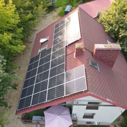 RAMZES Technologie Diamentowe Paweł Purzycki - Widok z góry na dom z panelami fotowoltaicznymi na dachu z czerwonej dachówki bitumicznej, obok komin z cegły, otoczony zielenią drzew.