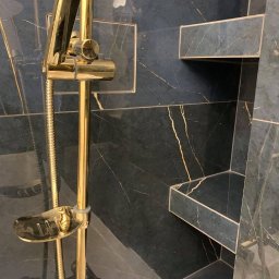 JAZZ BUD MICHAŁ BŁASZCZYŃSKI - Wykończona łazienka z czarnymi płytkami imitującymi marmur z złotymi żyłami, złota armatura prysznicowa i wnęki w ścianie wyłożone tą samą płytką.