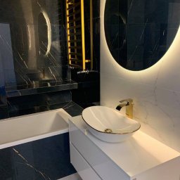 JAZZ BUD MICHAŁ BŁASZCZYŃSKI - Nowoczesna łazienka z czarnymi płytkami imitującymi marmur, białymi płytkami imitującymi marmur, owalną umywalką nablatową z elementami złota, baterią w kolorze złota i grzejnikiem drabinkowym...