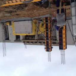 Wznoszenie ścian z bloczków Ytong na budowie domu, widoczne szalunki kolumn, zbrojenie i pracownik w tle.