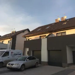 Szeregówka domów jednorodzinnych z antenami satelitarnymi na dachach, zaparkowany samochód osobowy i dostawczy z reklamą firmy.