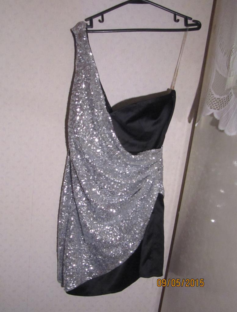 Czarno-srebrna, cekinowa sukienka mini na wieszaku, z asymetrycznym dekoltem i datą 09/05/2015 w prawym dolnym rogu, sugerująca użycie.