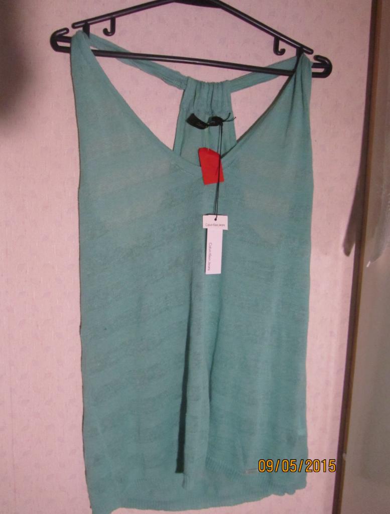 Miętowa bluzka Calvin Klein Jeans na wieszaku z metką, na tle ściany z datą 09/05/2015 w prawym dolnym rogu. Ubranie używane, okazja.