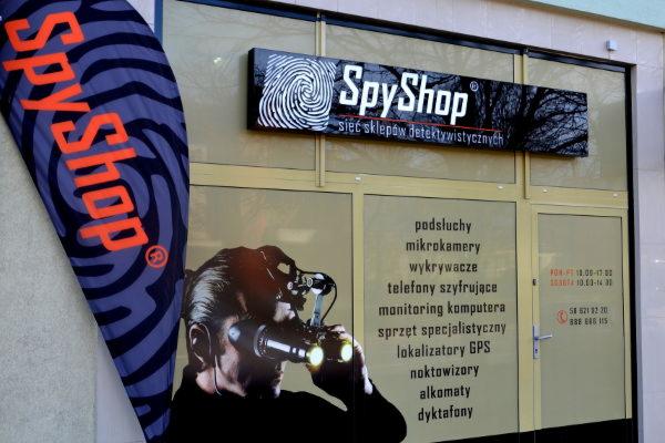 Fasada sklepu detektywistycznego SpyShop z logo, flagą i naklejkami reklamowymi na szybach w Gdyni.