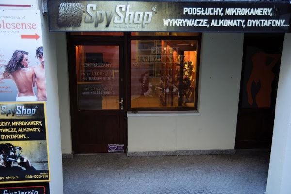 Fasada sklepu 'Spy Shop' w Krakowie, oferującego podsłuchy, mikrokamery, wykrywacze i dyktafony, z widoczną witryną i plakatem reklamowym.