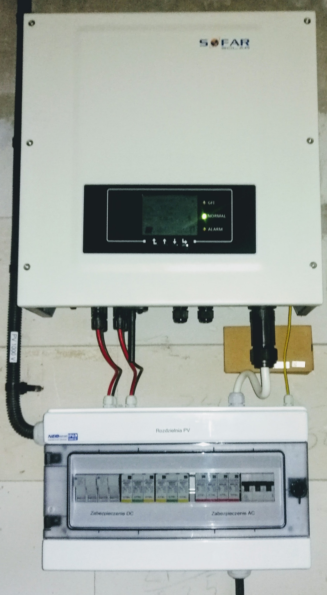 Biała obudowa falownika Sofar Solar zamontowana nad skrzynką rozdzielczą PV z widocznymi zabezpieczeniami DC i AC, przewody w peszlu.