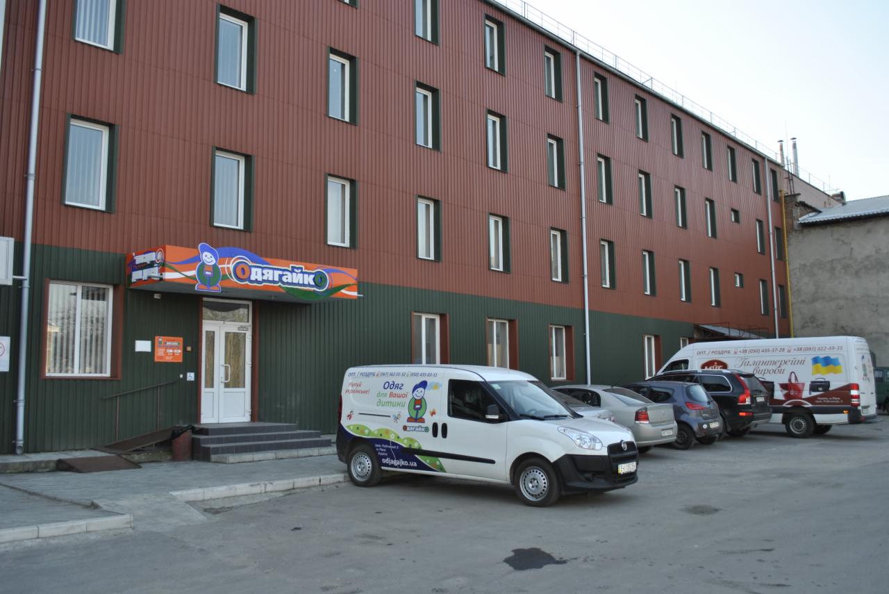 Budynek firmy odzieżowej dla dzieci 'Odyagayko' z zaparkowanym firmowym vanem z logo i informacjami kontaktowymi. Widok z zewnątrz, dzień.
