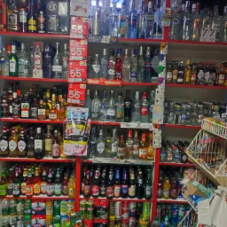 Półki sklepowe wypełnione różnorodnymi butelkami alkoholi, w tym wódki, piwa i whisky, z widocznymi cenami i materiałami reklamowymi.