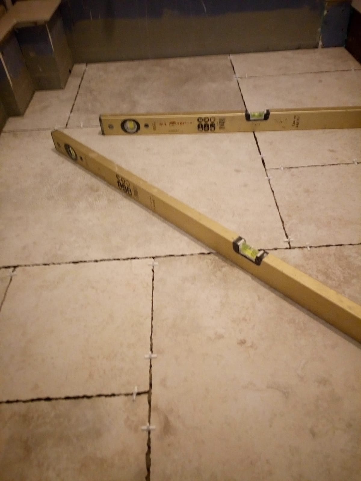 Ułożone beżowe płytki podłogowe z poziomnicami i krzyżykami dystansowymi w trakcie prac wykończeniowych w łazience.