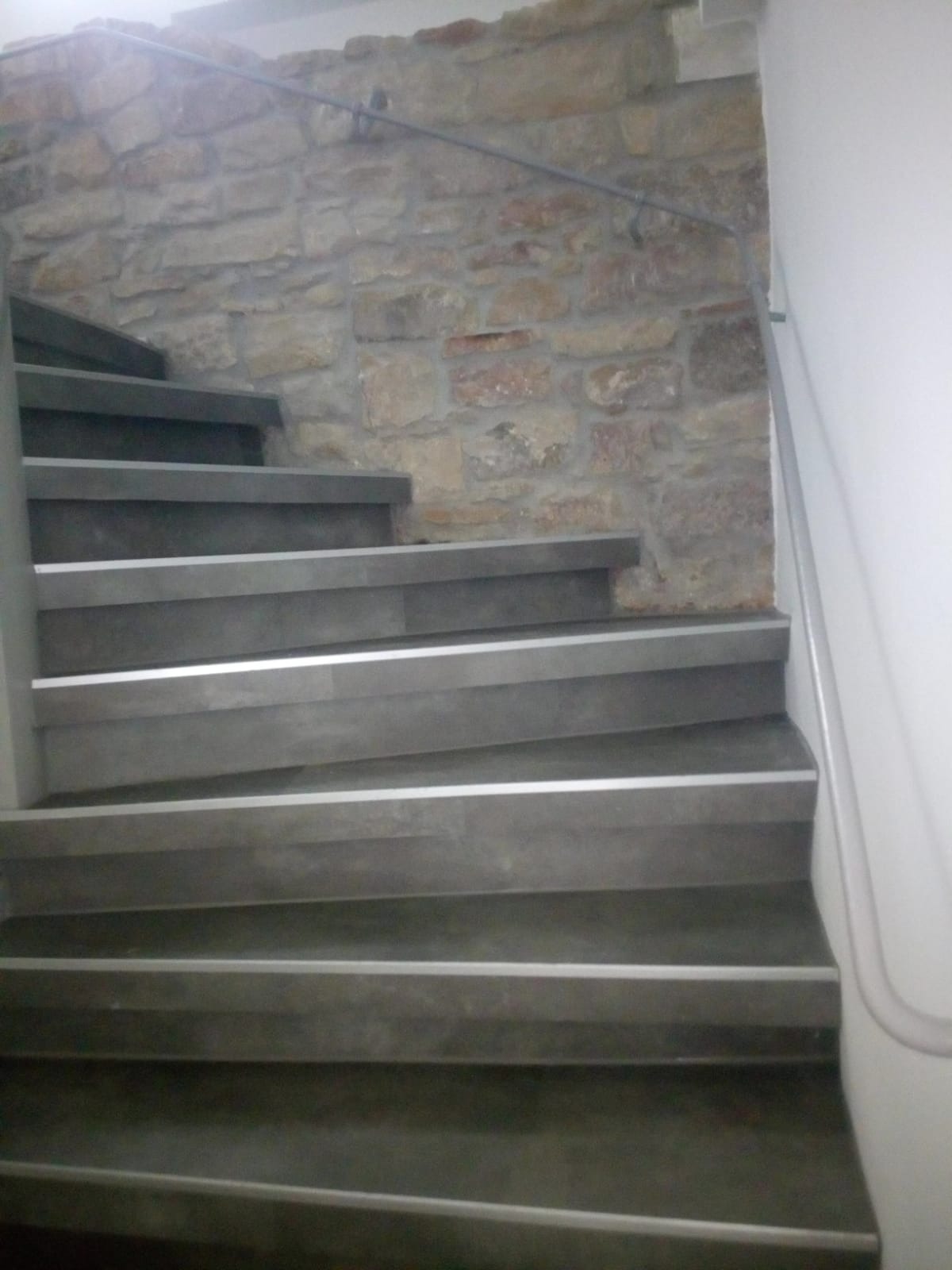 Schody z szarego kamienia z metalowymi krawędziami, ściana z kamienia naturalnego, poręcz ze stali nierdzewnej, ujęcie z dołu.