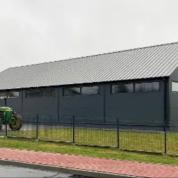 Gotowa hala przemysłowa w Sobuczynie z szarej płyty warstwowej i blachy trapezowej, widoczny traktor John Deere na tle ogrodzenia.