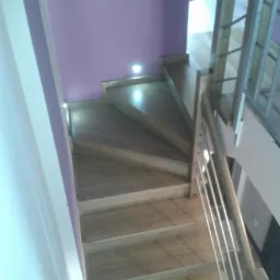 Klatka schodowa z drewnianymi stopniami i metalową balustradą, oświetlona punktowymi lampami w ścianie, widok z góry.