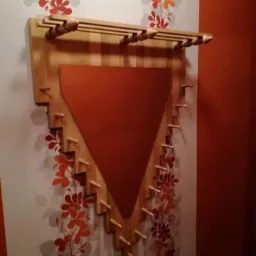 Nietypowy wieszak ścienny z drewna z trójkątnym lustrem w kolorze miedzi, umieszczony na ścianie z kwiatowym wzorem.