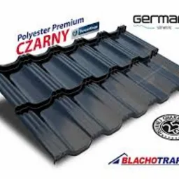 Czarna dachówka Germania z logo Blachotrapez, z widocznym połyskiem. Ujęcie z bliska, prezentujące fakturę i kształt. Na białym tle.