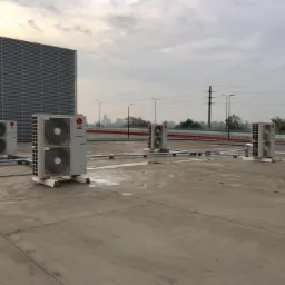 Instalacja klimatyzacji przemysłowej: cztery jednostki zewnętrzne LG z podwójnymi wentylatorami na betonowym dachu, widoczne przewody i tło miejskiego krajobrazu pod pochmurnym niebem.