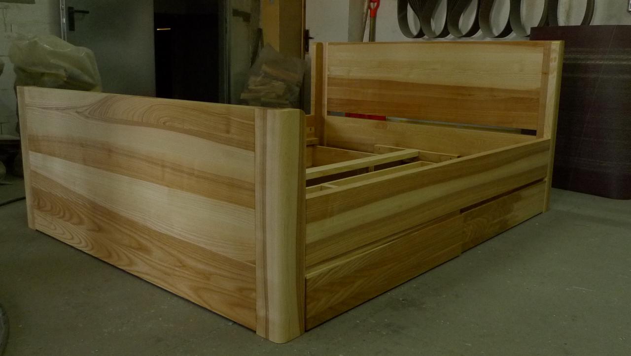 Rama łóżka z jasnego drewna w trakcie montażu, widoczne elementy konstrukcyjne i naturalny rysunek drewna, w tle warsztat stolarski.