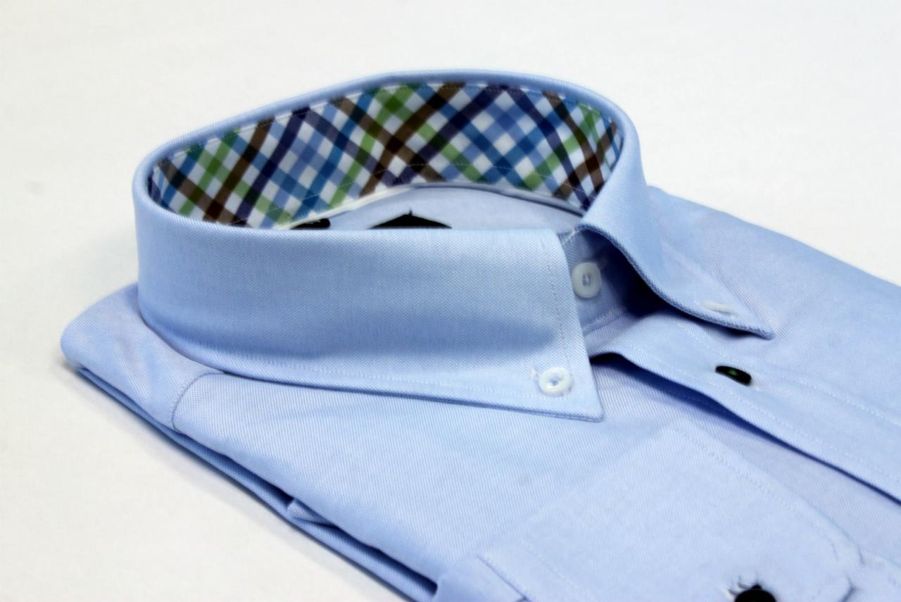 Jasnoniebieska, złożona koszula męska z kołnierzykiem button-down, wykończonym od wewnątrz wzorem w kratę.