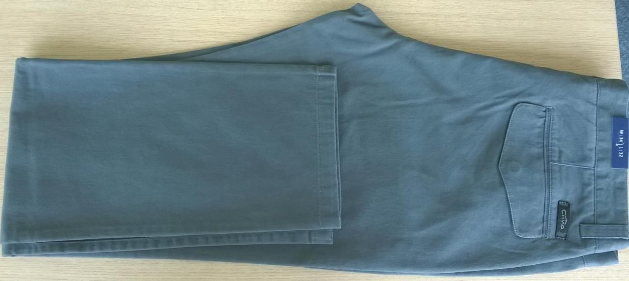 Niebiesko-szare spodnie młodzieżowe, złożone na drewnianym blacie, widoczna metka z rozmiarem W 34 L 32 oraz logo marki CHIAO.