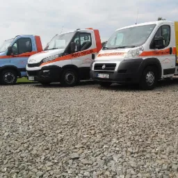 Trzy lawety pomocy drogowej różnych modeli (Iveco i Fiat) stojące na żwirowym parkingu, z widocznymi numerami telefonów i oznaczeniami firmy CAR-MAT.