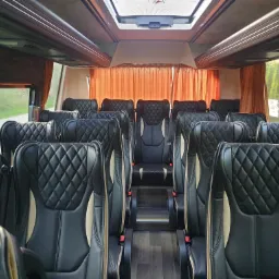 Wnętrze luksusowego busa z czarnymi, pikowanymi skórzanymi fotelami z beżowymi wstawkami i pomarańczowymi zasłonami w oknach.