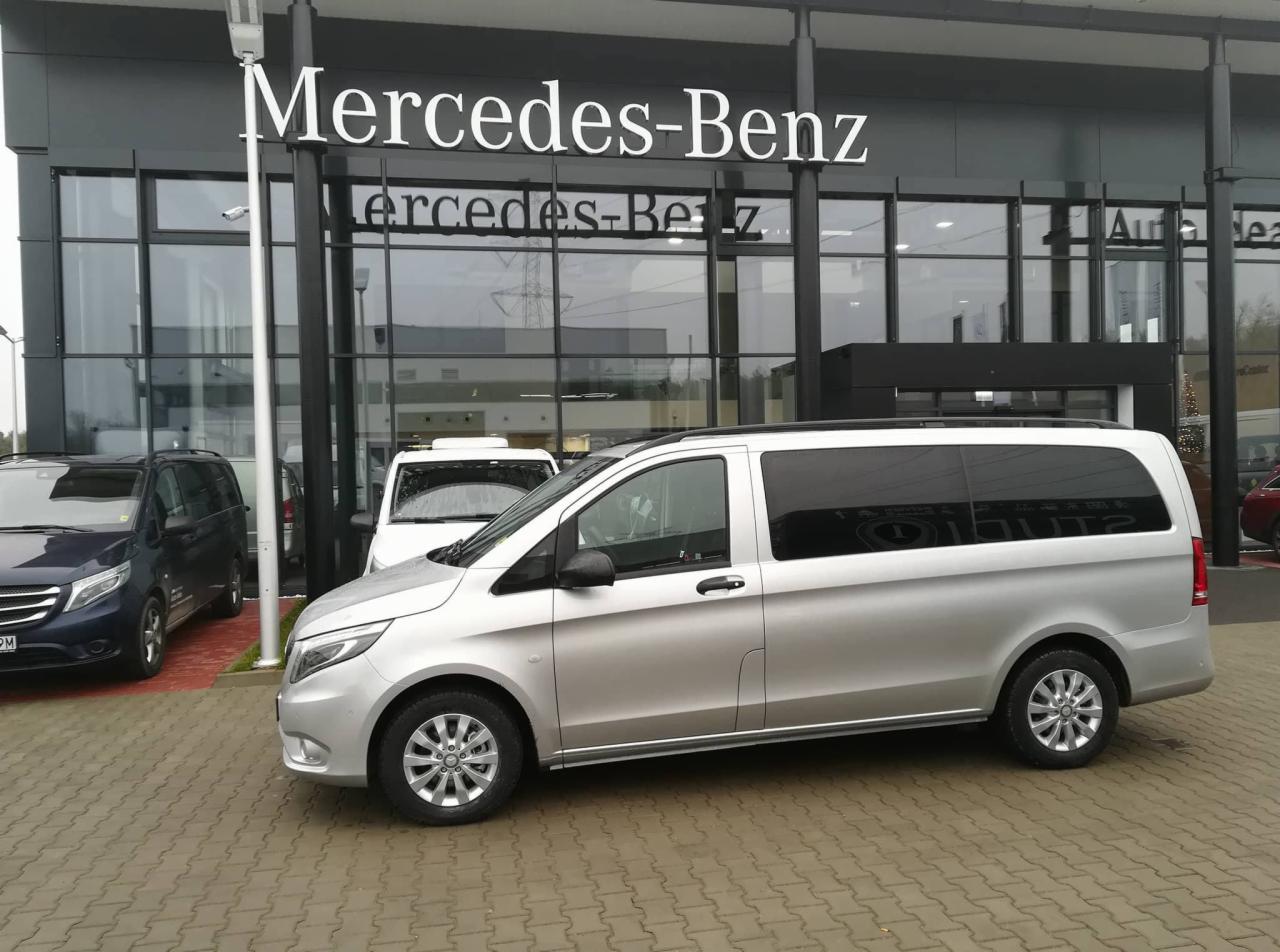 Srebrny Mercedes-Benz Vito z przyciemnianymi szybami, zaparkowany przed salonem Mercedes-Benz na brukowanym placu.