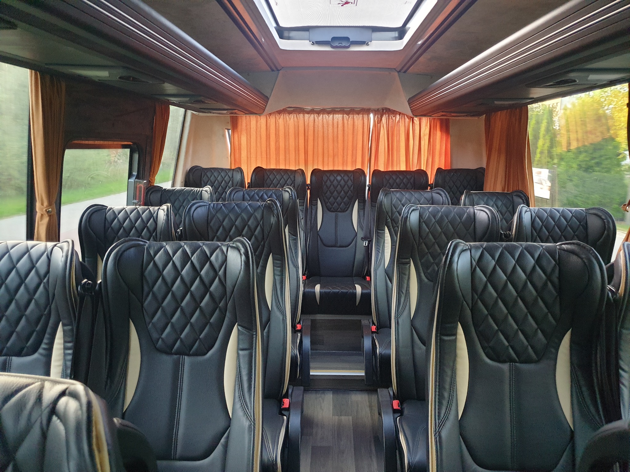 Wnętrze luksusowego busa z czarnymi, pikowanymi skórzanymi fotelami z beżowymi wstawkami i pomarańczowymi zasłonami w oknach.